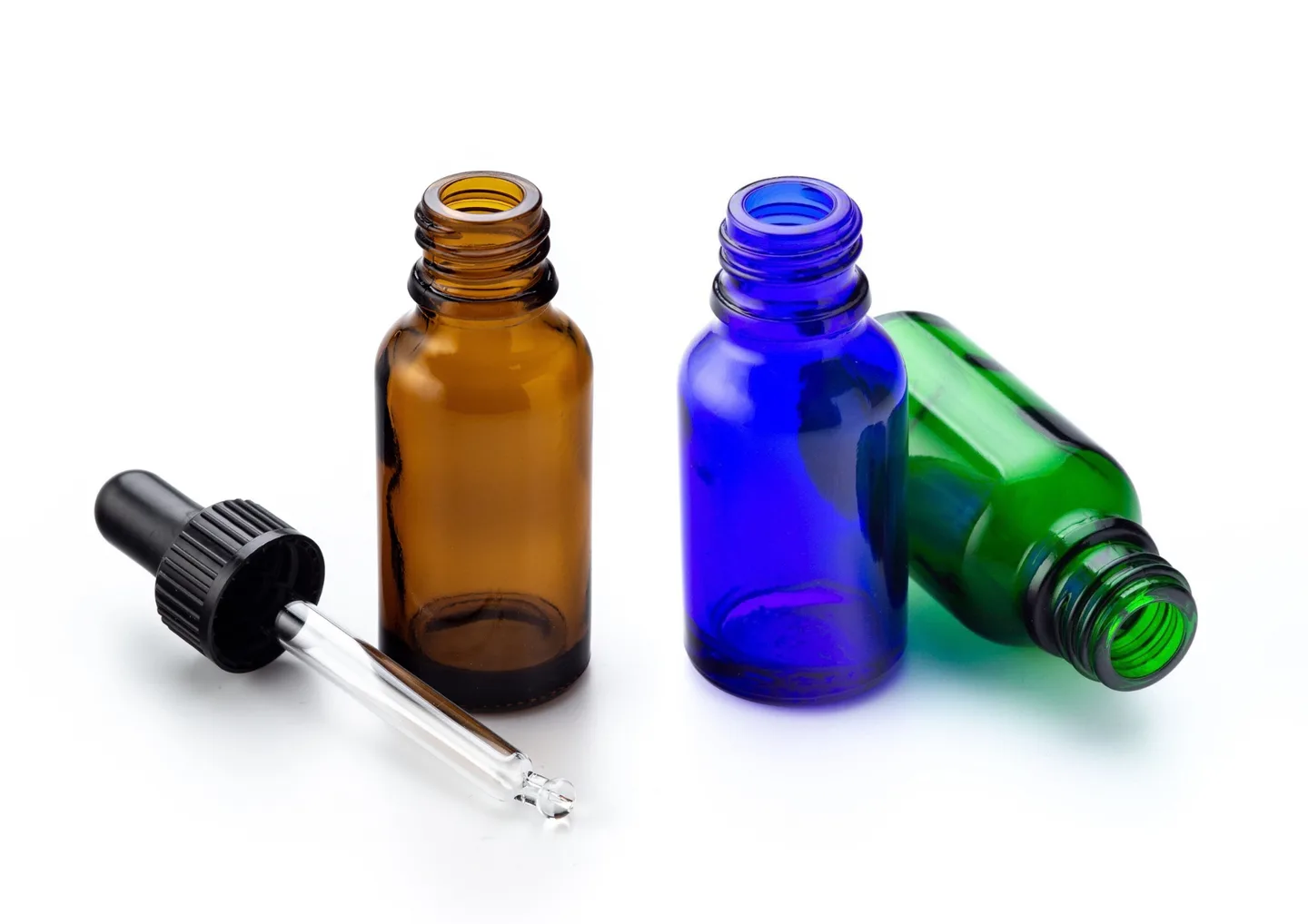 A glass pipette with a black plastic neck and bulb, as well as an amber, blue, and green glass dropper bottle sit on a white tabletop against a white background.